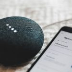 turned-on charcoal Google Home Mini and smartphone